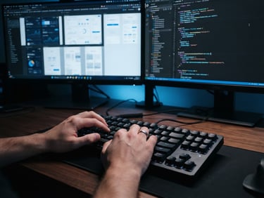 Close-up shot of hands typing code on a mechanical keyboard, high-fidelity UI mockups visible on a clean dual-monitor setup in a modern workspace, cool blue studio lighting, sharp focus, 35mm lens