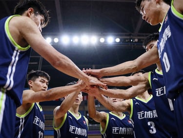 Candid team huddle of youth basketball players placing their hands together, high-contrast stadium lighting, deep blue jerseys, action freeze-frame.