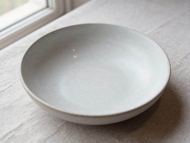 Overhead close-up of a single plated dish on a matte ceramic bowl — restaurant setting, pale linen surface, natural window light, minimal Scandinavian composition