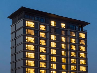 Modern residential building exterior at dusk, clean vertical lines, deep blue hour sky, warm lights glowing from large windows