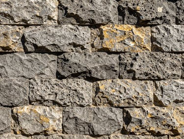 Structured stone wall made of large textured grey rocks, precise masonry work, sunlight highlighting textures
