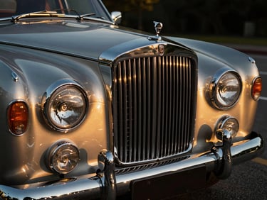 Close-up of a vintage luxury car's chrome grille and headlight, highly polished, golden hour light reflecting off the metal, wide-angle lens.
