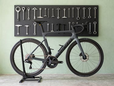 Side view of a clean, organized bicycle repair stand, a carbon frame road bike mounted, tools arranged neatly on a magnetic strip in the background