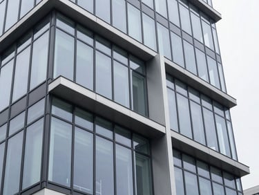 Architectural detail of a modern glass and steel office facade, sharp angles, high-contrast overcast daylight, cool silver-gray tones.