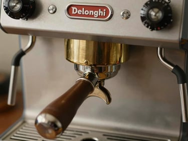 Close-up overhead of a Delonghi espresso machine group head, brass portafilter locked in, even studio light revealing machined metal detail