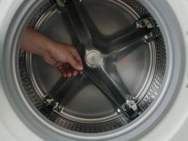 Close-up overhead view of washing machine drum interior, a technician's hand adjusting a belt component, even studio light, muted gray tones