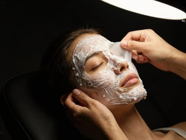 Hands applying a mask to a face under a warm studio light, editorial clinical photography, deep black background, sharp focus