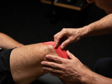 Therapist applying kinesiology tape to an athlete's knee, precise hands-on technique, dramatic low-key lighting, 35mm