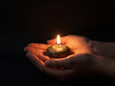A quiet, respectful therapeutic setting, warm candle light casting gold glow on hands holding a symbolic smooth stone, dark background