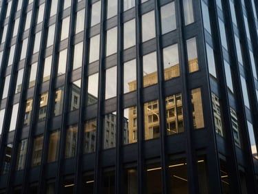 Wide architectural shot of a modern corporate building facade reflecting overcast daylight, abstract geometric shadows, deep navy and muted gold tones, 35mm