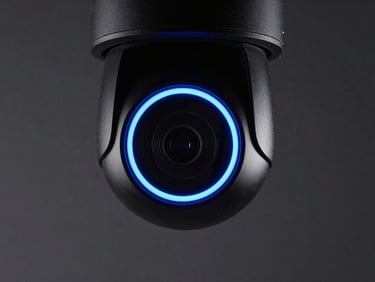 Close-up of a sleek black dome IP camera with a glowing blue status ring, dark graphite background, sharp studio lighting