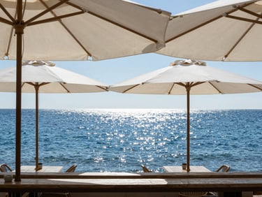 A minimalist seaside cafe in Costa Brava, white canvas umbrellas, sparkling blue sea in the background