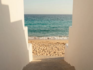 View of a path or stairs leading directly from a cliffside property to the sandy beach and clear turquoise waters of Playa Lagun. Soft coastal light.