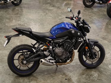 Overhead three-quarter view of a Yamaha MT-07 on polished concrete showroom floor under studio strobe, dark blue and black bodywork, engine fins visible, no rider