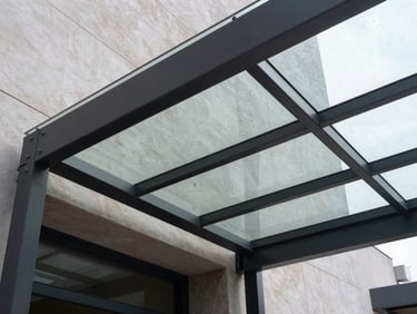 Modern minimalist entrance canopy with structural steel supports and clear laminated glass, low-angle shot looking up.