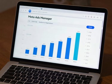 Tight crop of a laptop screen showing Meta Ads Manager with audience breakdown charts and ROAS column highlighted in cool studio light, desk surface visible at edges, no people