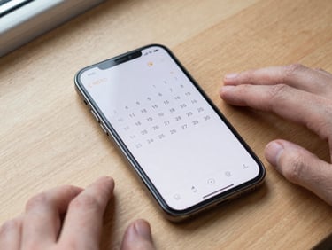 Overhead shot of an Android phone displaying a clean calendar widget on a home screen, placed on a light wooden desk, natural window light, no clutter, fingers resting beside the device