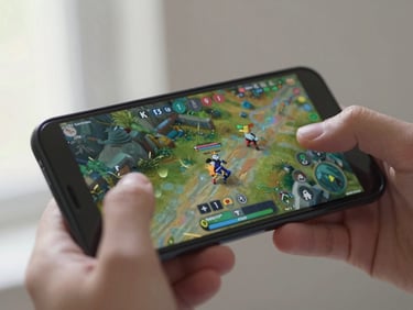 Close-up of an Android phone held in a hand mid-game, touch controls visible on a vivid game interface, natural daylight from the left, motion blur on thumb suggesting active play