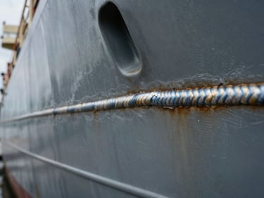 Macro close-up of heavy marine engineering, focusing on clean weld lines and structural steel plates of a ship's hull.