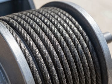 Close-up of a new garage door lift cable, taut and clean, against a dark metal drum, bright natural daylight.