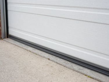 Technician installing new rubber weather stripping along the bottom edge of a garage door, natural daylight, focus on the seal.