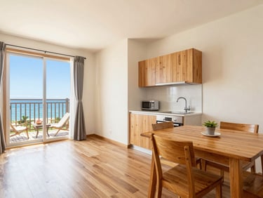Cozy junior suite with small kitchenette, dining table, warm teak wood styling, bright daylight.