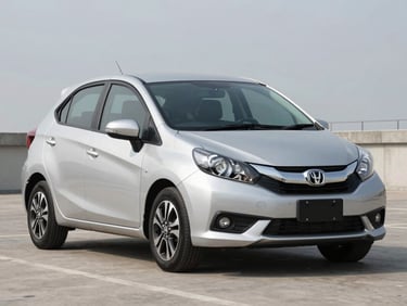 Three-quarter front view of a Toyota Avanza or Honda Brio sedan parked on smooth concrete in bright diffused daylight, full vehicle visible, realistic silver-white color, no reflective glare