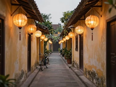Tight environmental frame, soft morning light on a quiet Hoi An lantern-lit alley at dawn, warm amber lanterns unlit against pale plaster walls, a bicycle leaning at the far end, no people, overcast natural light