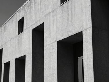 Cinematic black and white architectural shot of a minimalist concrete building facade under harsh sunlight, deep black shadows, elegant luxury aesthetic.