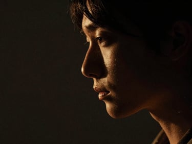Moody editorial close-up of a person's profile in deep shadows, high-contrast chiaroscuro lighting, subtle warm gold highlight.