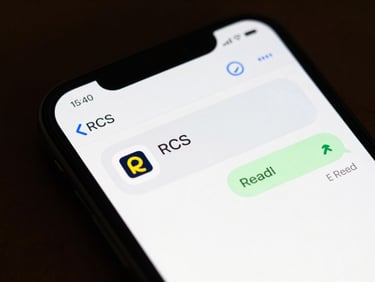 Close-up of an Android phone screen displaying an RCS chat message with a brand carousel, action buttons, and a read receipt timestamp, even studio lighting, UI elements sharp and legible