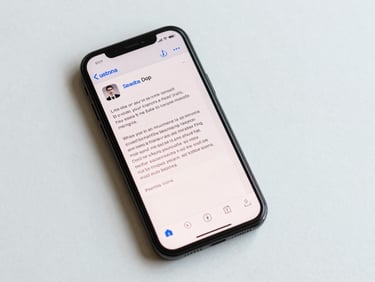 Overhead flat-lay of a basic handset screen showing an SMS inbox with a campaign message from a brand sender ID, bright daylight, clean white surface, text readable at full scale