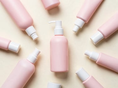 Overhead flatlay of pastel pink skincare bottles and tubes, soft morning light, cream background, 35mm