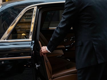 Close-up of a sharply dressed chauffeur in a dark suit opening a rear passenger door of a luxury car