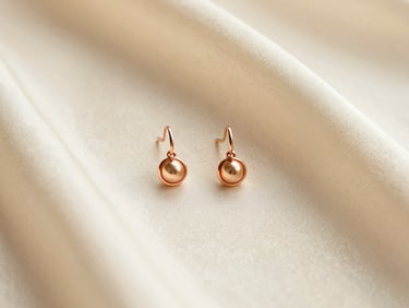 Macro flat lay of a detailed rose gold bridal earring resting on a soft ivory silk fabric, warm diffused lighting catching the metallic edges.