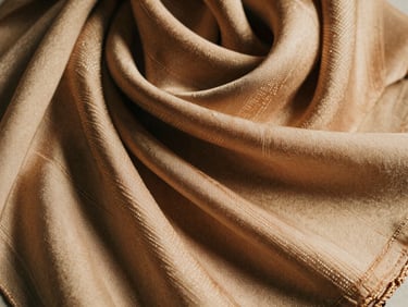 Close-up of a silk scarf with a heritage weave pattern, delicate texture, warm sand nude, 35mm film.