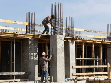 Real active construction site in Colombia, workers pouring concrete into a foundation column under bright daylight, steel rebar framework visible, realistic architectural details, 35mm