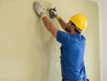 A technician in a vivid cobalt blue polo shirt and dark gray pants paints the exterior stucco wall of a premium Florida estate with a professional roller, bright Florida daylight.