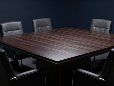 Mesa de conferencia vacía de madera oscura pulida con sillas de cuero, luz lateral dramática que resalta texturas, tonos fríos.