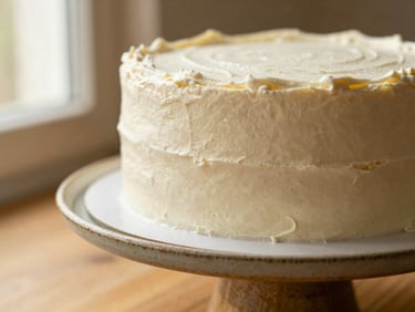 Close-up of a minimalist custom cake with delicate white frosting on a rustic ceramic stand, soft warm lighting