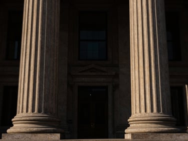 Symmetrical architectural shot of courthouse pillars, low-key dramatic side-lighting, deep brown and gold tones, high contrast, 35mm