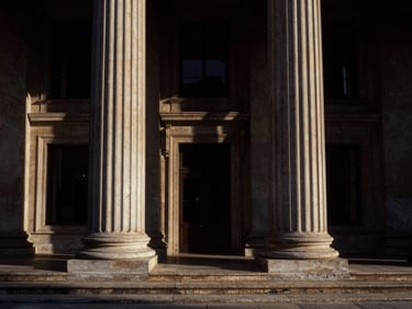 Symmetrical wide-angle architectural shot of neoclassical courthouse pillars, dramatic side-lighting, deep bronze shadows, high contrast, 35mm