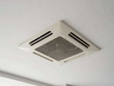 Overhead wide-angle shot of a ceiling cassette AC unit installed flush into suspended ceiling tiles, clean commercial interior, neutral daylight lighting, no people