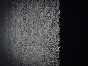 Extreme close-up of a concrete texture, dramatic lighting, high-contrast monochrome, hint of electric blue in the shadows, anamorphic lens.
