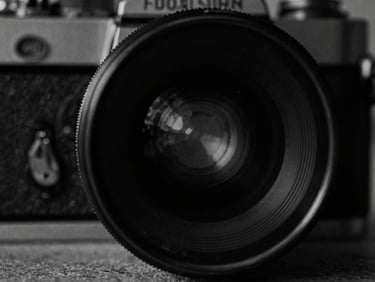 Close-up of a vintage film camera lens, high-contrast monochrome, moody low-key lighting, 35mm grain, cinematic film photography