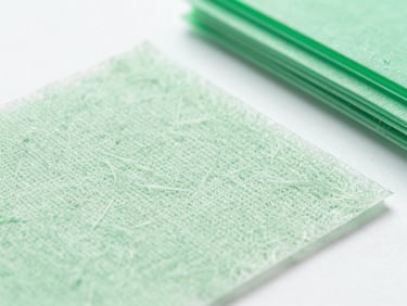 Macro shot of textured biodegradable spunlace nonwoven fibers under bright clinical white studio light, detailed fabric structure, sterile white laboratory light, fresh green tones, sharp focus, 35mm