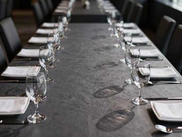 Dead-on eye-level architectural perspective of a corporate gala table setup, deep charcoal tones, strict geometric alignment of glassware, sharp shadows.