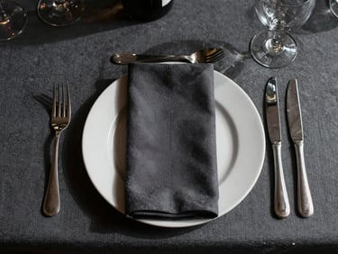 Overhead flat-lay of a minimalist corporate gala table setting, sharp shadows, deep charcoal accents, natural light.