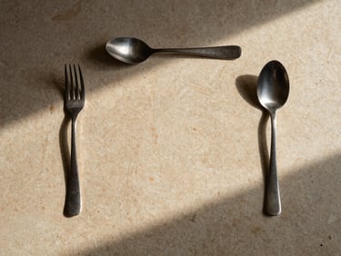 Strictly overhead flat-lay of a minimalist table setting on warm stone, precise placement of cutlery and single-source directional light.