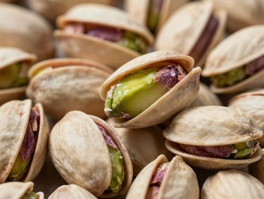 Extreme close-up of raw unshelled pistachios in a cargo container, bright daylight reflecting off natural green and purple skins